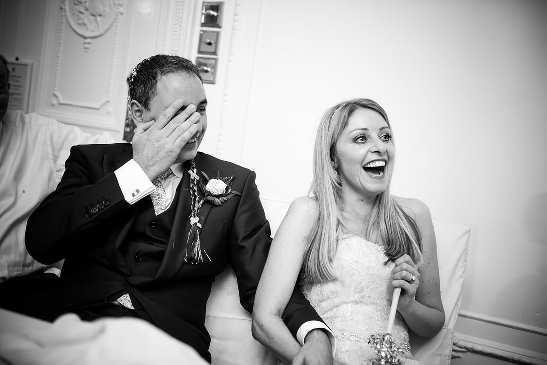Black and white image of the bride and groom laughing during the speeches at their wedding at Taplow House, Buckinghamshire.