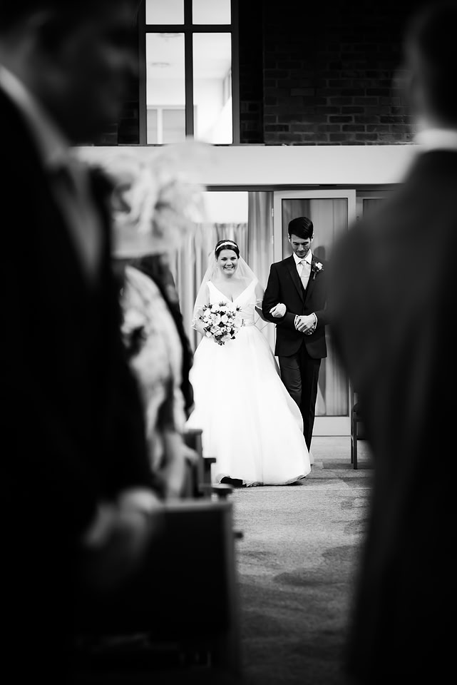 Black and white image of the bride walking down the aisle towards her groom.