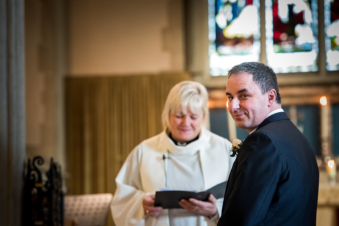 Image of the groom glancing back at the bride as she walks down the aisle at a wedding in Buckinghamshire.