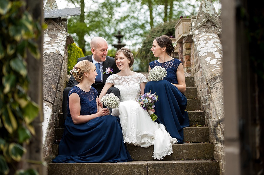A photograph of Ross & Mair with their bridesmaids sitting on the steps at Soughton Hall