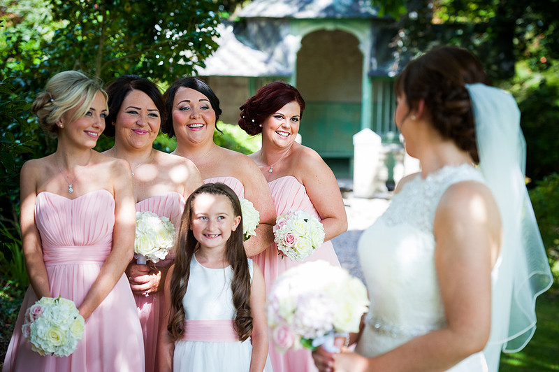 The bridesmaids smiling at the bride in the gardens during a wedding in Chateaux Rhianfa, Anglesey. Wedding Photographer, Celynnen Photography