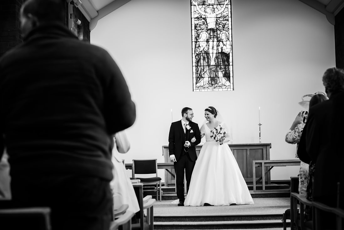 Black and white image of the bride and groom about to leave the ceremony as husband and wife.