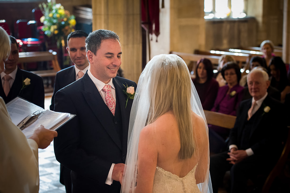 Image of the groom smiling at the bride during their wedding ceremony in a church in Buckinghamshire.