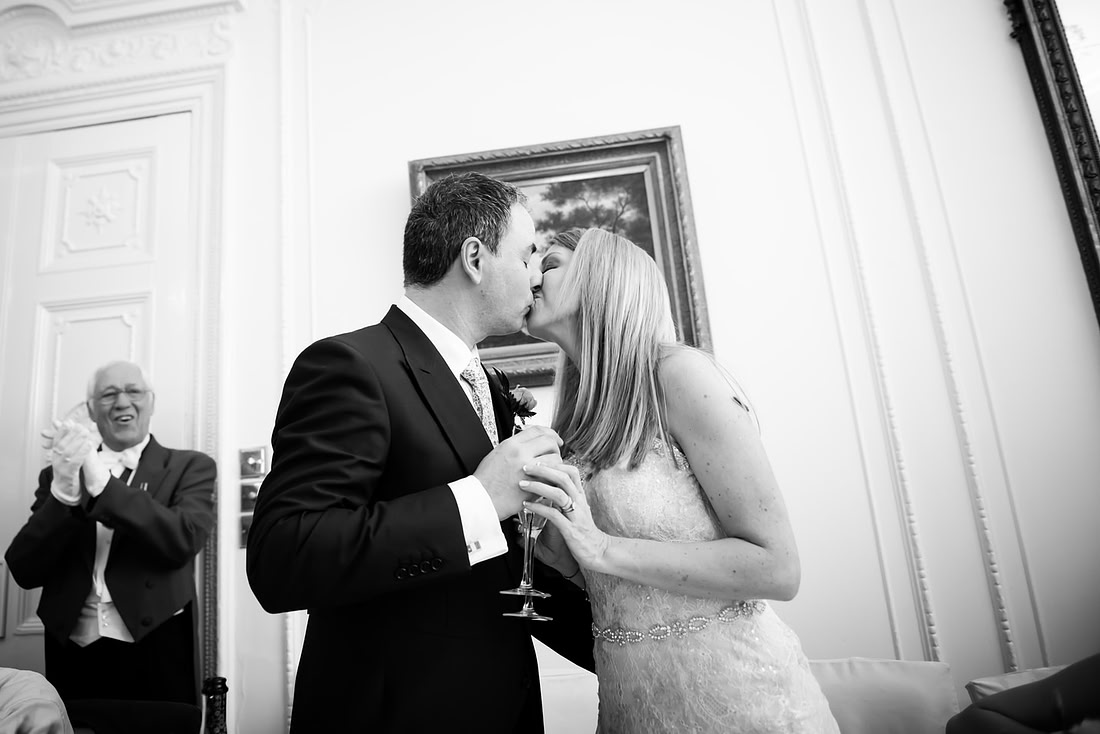 Black and white image of the bride and groom kissing during the speeches at their wedding at Taplow House, Buckinghamshire.
