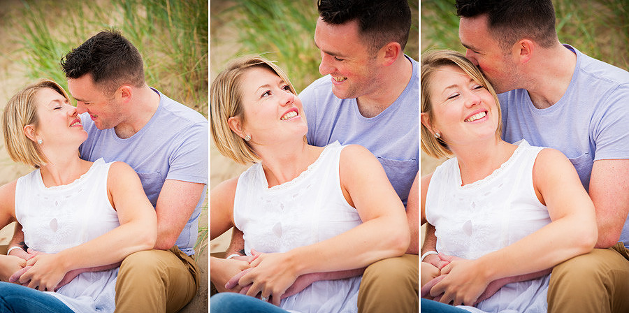 Young couple kissing and laughing, sitting on sand dunes during their portrait session on talacre beach near mold in North Wales
