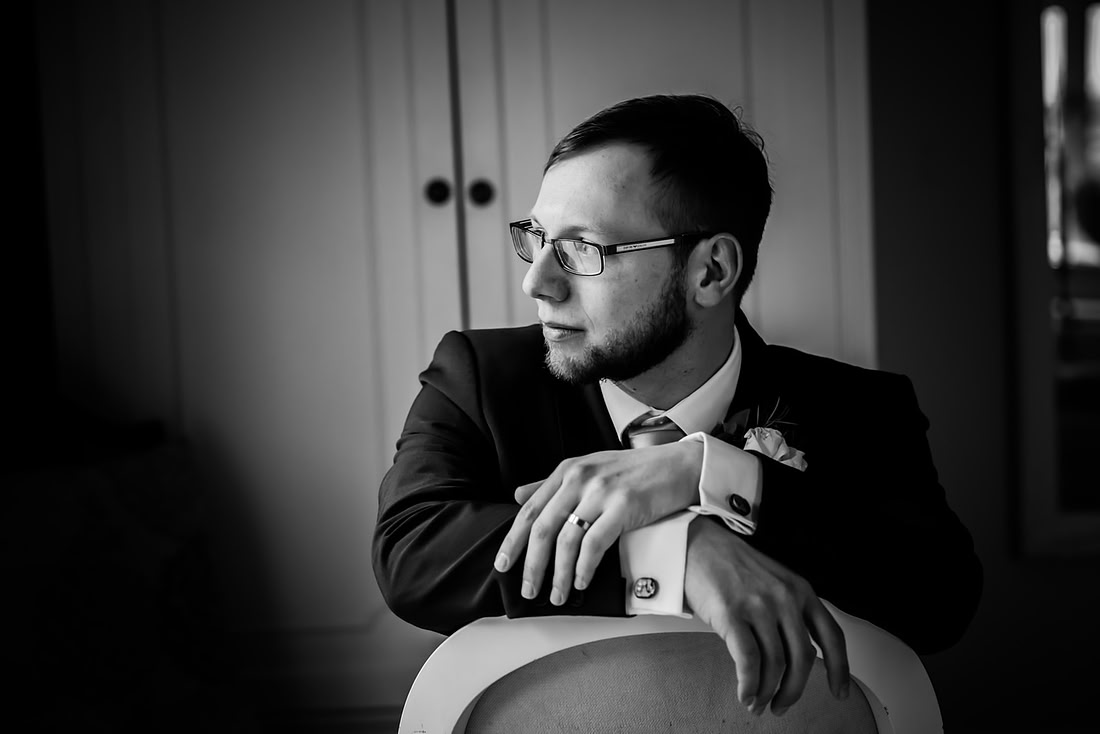 Black and white image of the groom sitting and looking at of the window at a wedding at Mere Brook House.