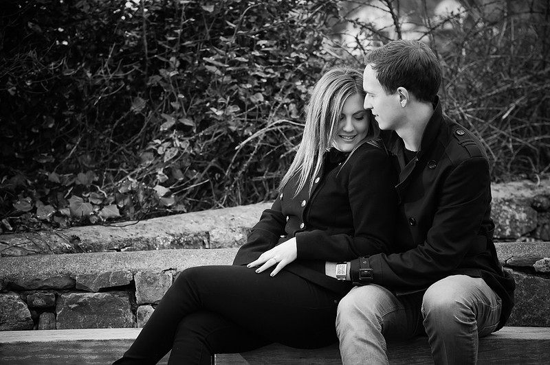 Black and white image of an engaged couple sitting on a bench together during their pre wedding shoot.