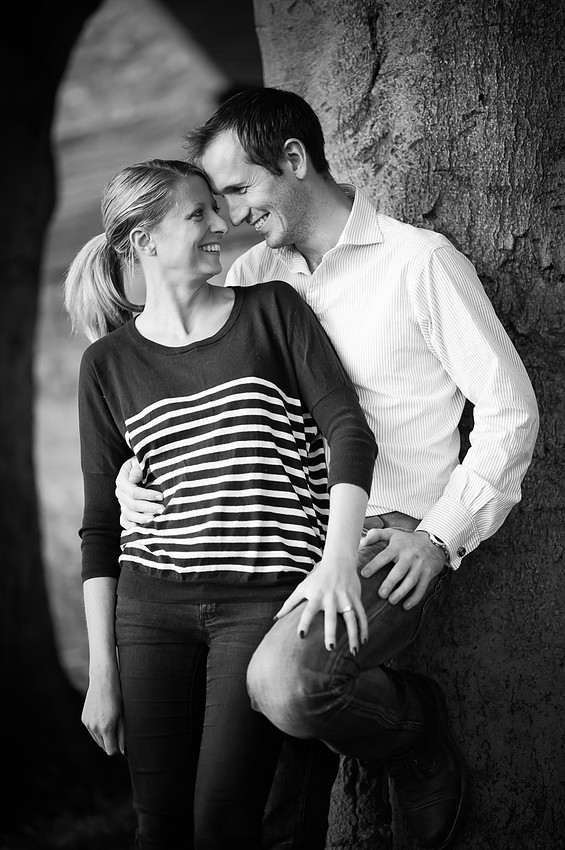 Black and white portrait of a couple leaning against a tree while smiling at each other, in Cheshire.
