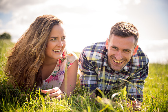A happy couple lying in the grass enjoying their pre wedding photoshoot in Cheshire, captured by Celynnen Photography