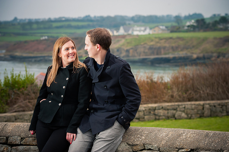 Photo of a couple leaning on a wall with beautiful scenery in the background.