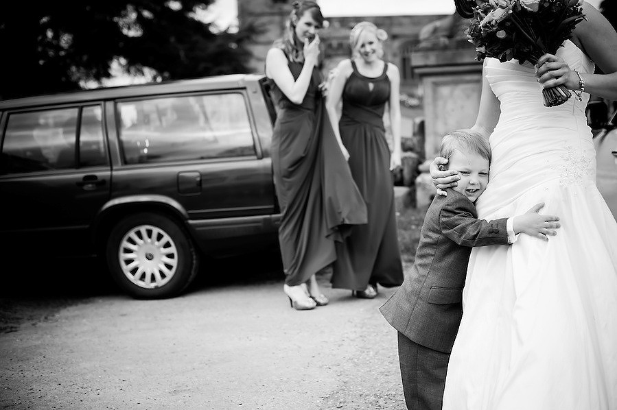 Black and white image of a young boy hugging the bride before the wedding ceremony