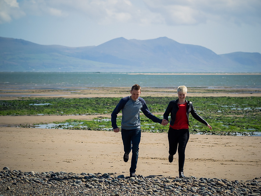 Photograph of Liz & Jason running on the beach at Newborough Forest & Warren in Anglesey, photographed by Celynnen Photography.