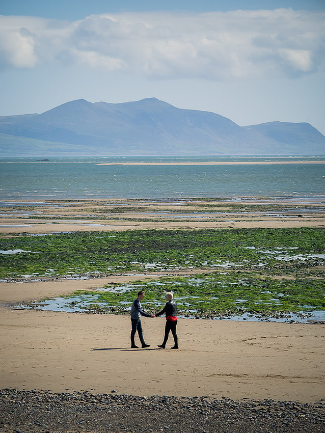 Photograph of Liz & Jason on the beach at Newborough Forest & Warren in Anglesey on their pre wedding shoot. Mountains & estuary in the background, photographed by Celynnen Photography.