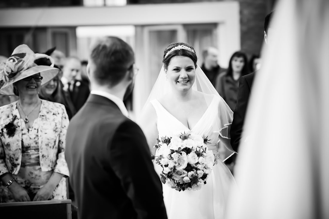 Black and white image of the bride smiling at her groom when she walks down the aisle.