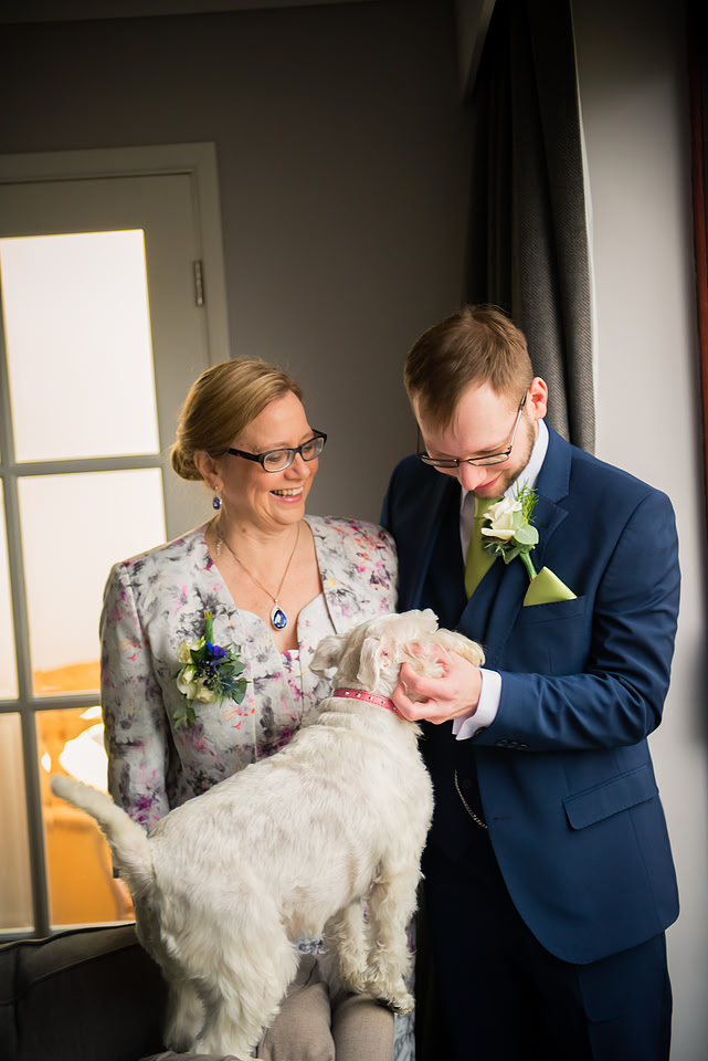 Image of the groom interacting with a dog while posing for a picture with his mum.