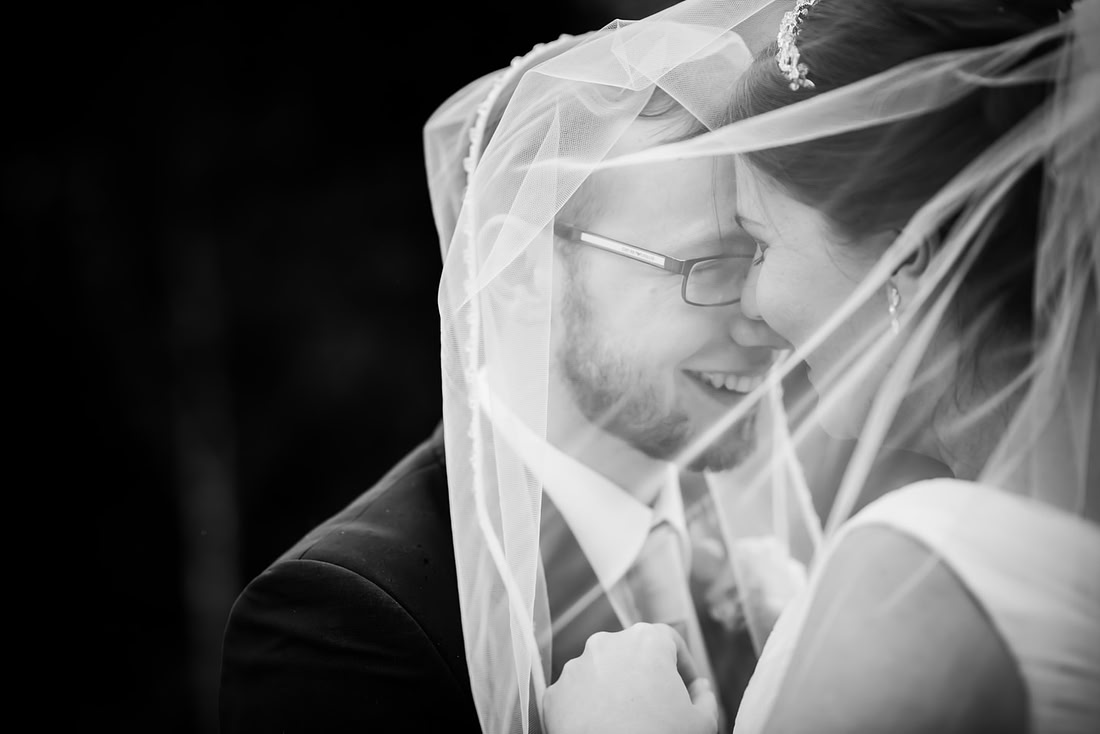 Black and white image of the bride and groom embracing each other under the bride's vale at a wedding at Mere Brook House.