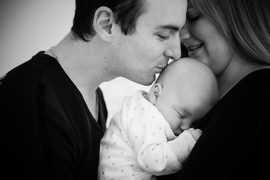 Black and white image of father kissing his newborn baby on the head 